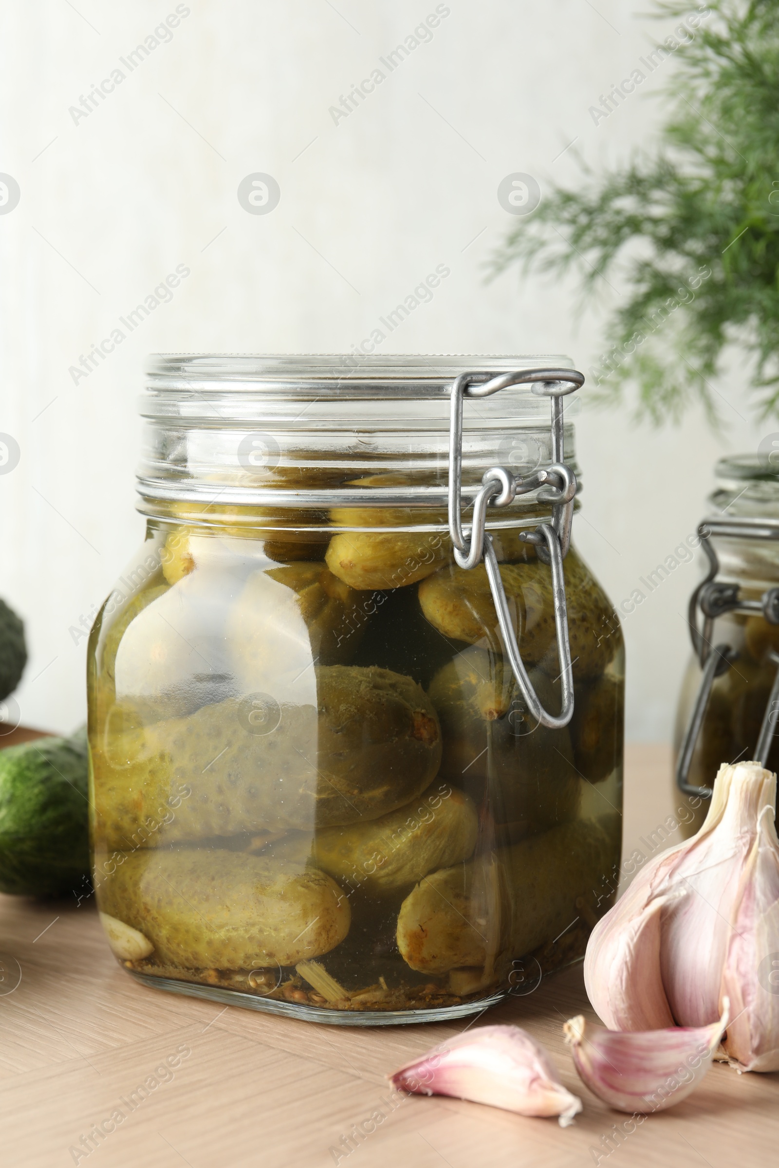 Photo of Pickled cucumbers in jar and garlic on wooden table, closeup