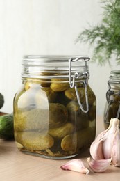 Pickled cucumbers in jar and garlic on wooden table, closeup