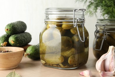 Photo of Pickled cucumbers in jars, peppercorns and garlic on wooden table, closeup