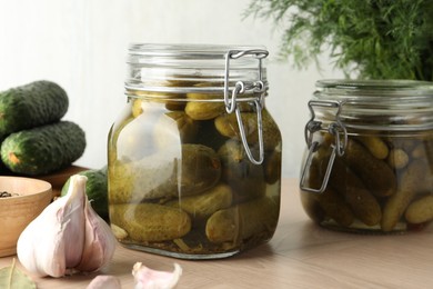 Pickled cucumbers in jars and garlic on wooden table, closeup