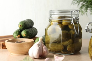 Pickled cucumbers in jar, peppercorns and garlic on wooden table, closeup