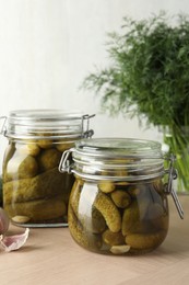 Photo of Pickled cucumbers in jars and garlic on wooden table