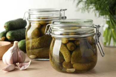 Photo of Pickled cucumbers in jars and garlic on wooden table, closeup