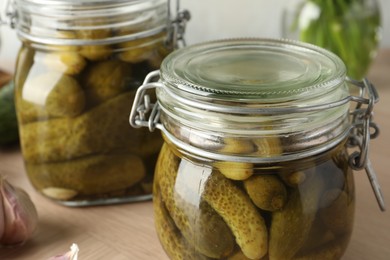 Pickled cucumbers in jars on wooden table, closeup