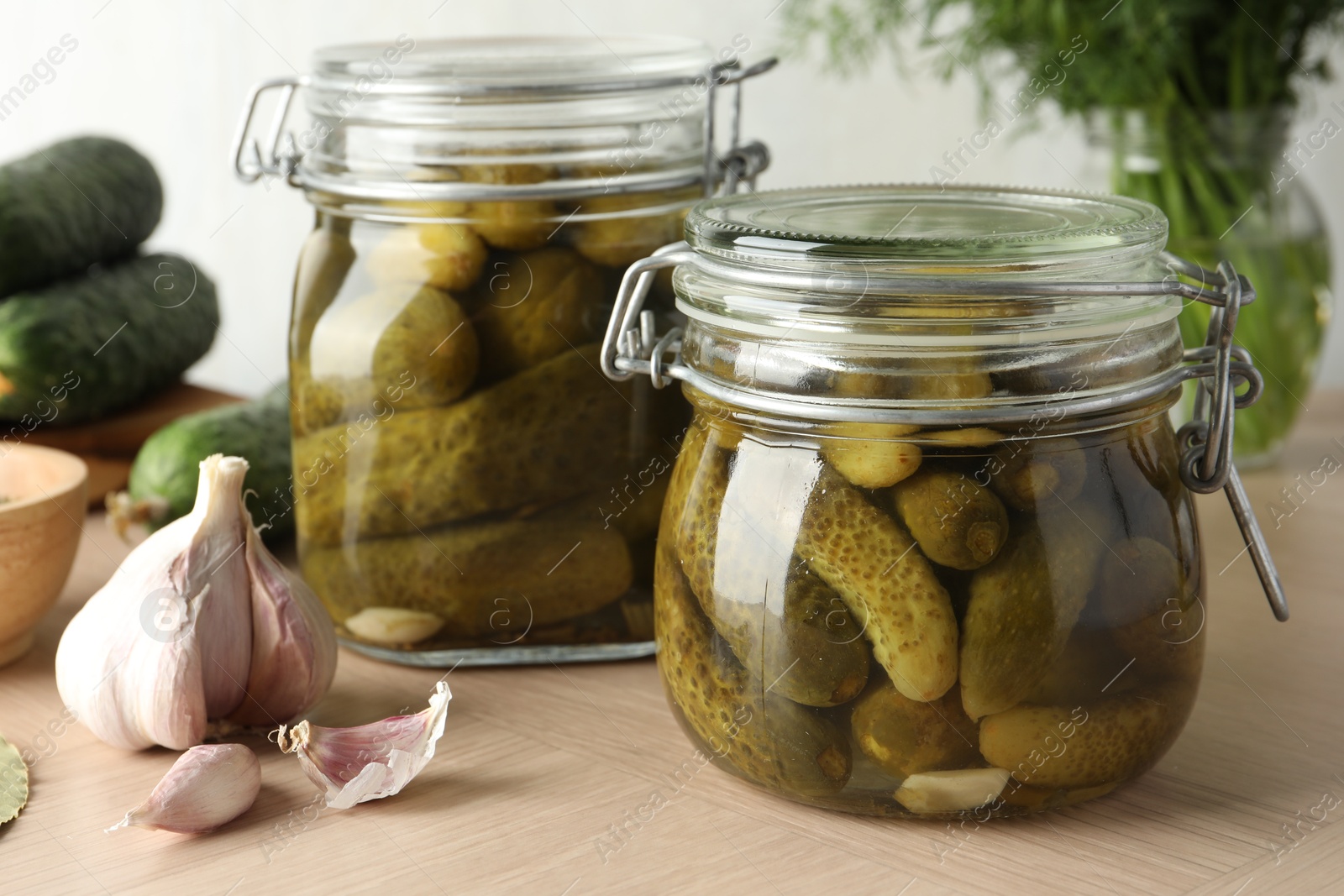 Photo of Pickled cucumbers in jars and garlic on wooden table, closeup