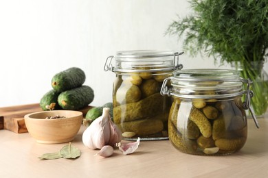 Pickled cucumbers in jars, garlic and bay leaves on wooden table