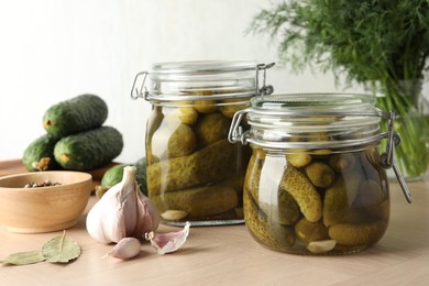 Pickled cucumbers in jars, garlic and bay leaves on wooden table