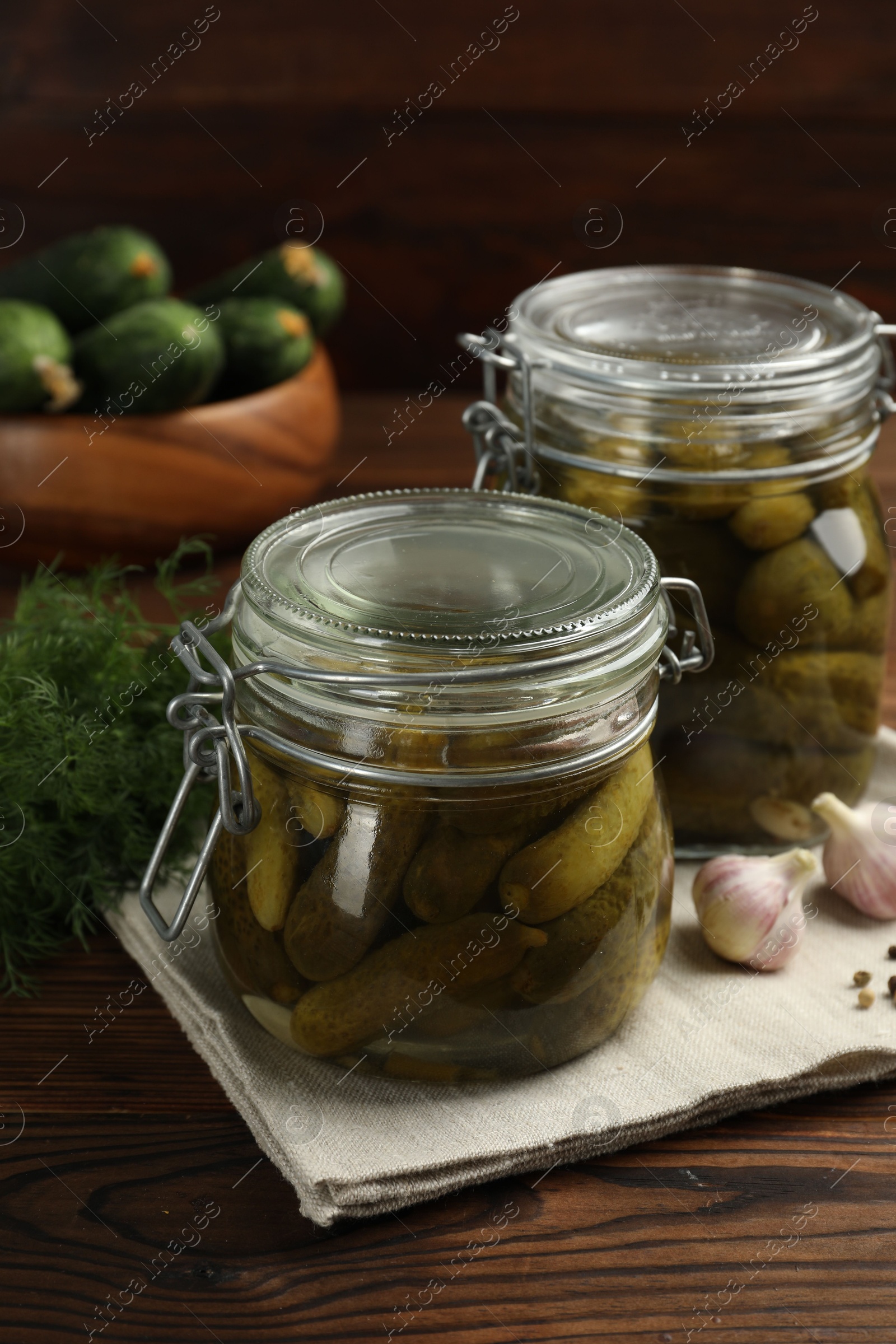 Photo of Pickled cucumbers in jars, garlic and dill on wooden table