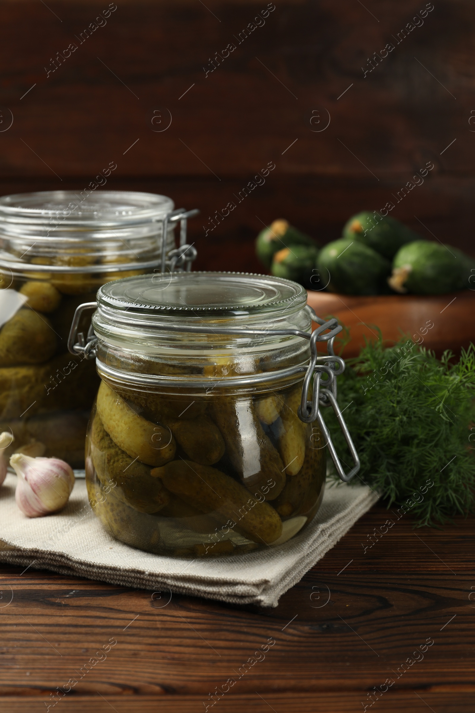Photo of Pickled cucumbers in jars, garlic and dill on wooden table