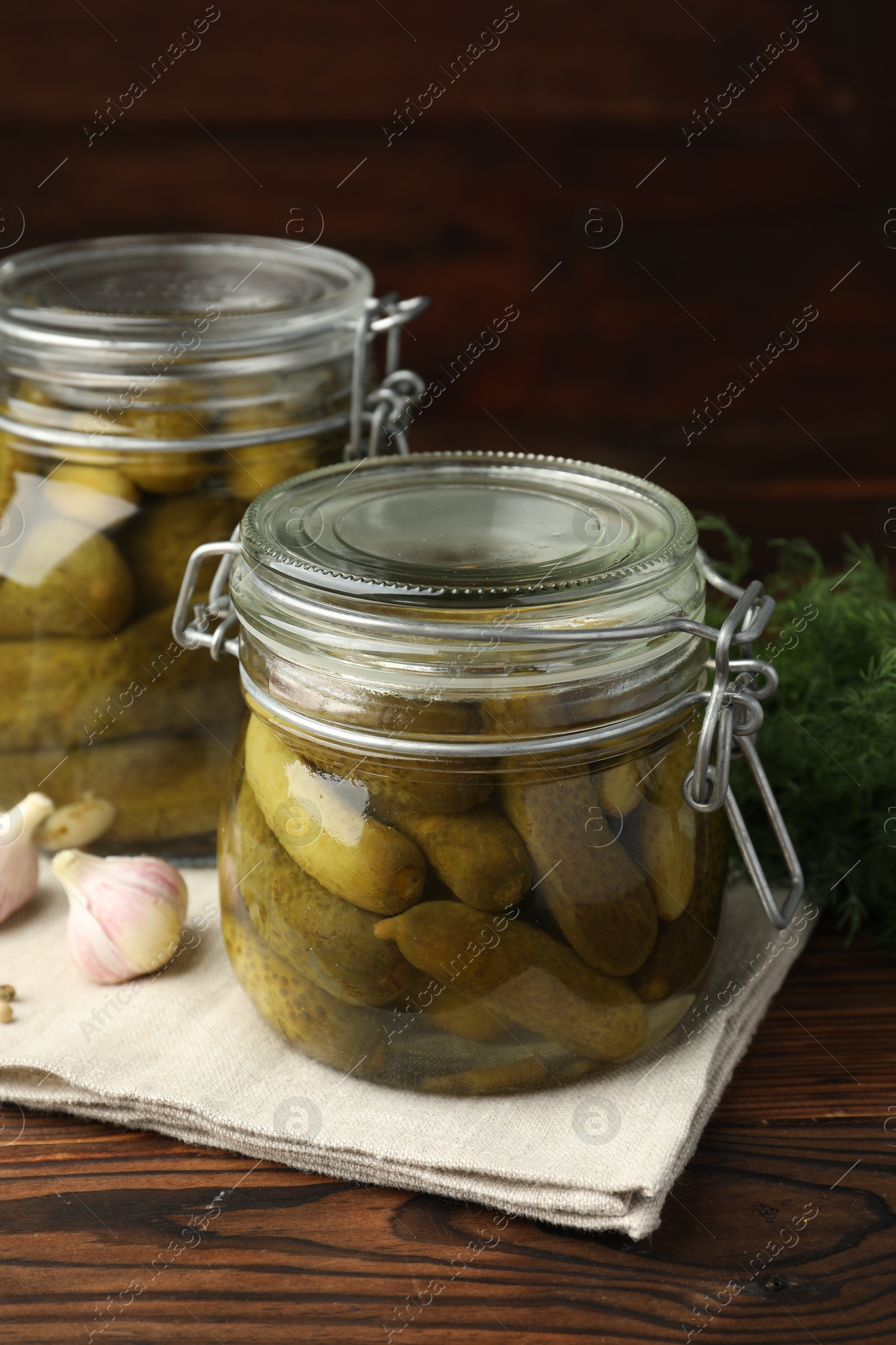 Photo of Pickled cucumbers in jars, garlic and dill on wooden table