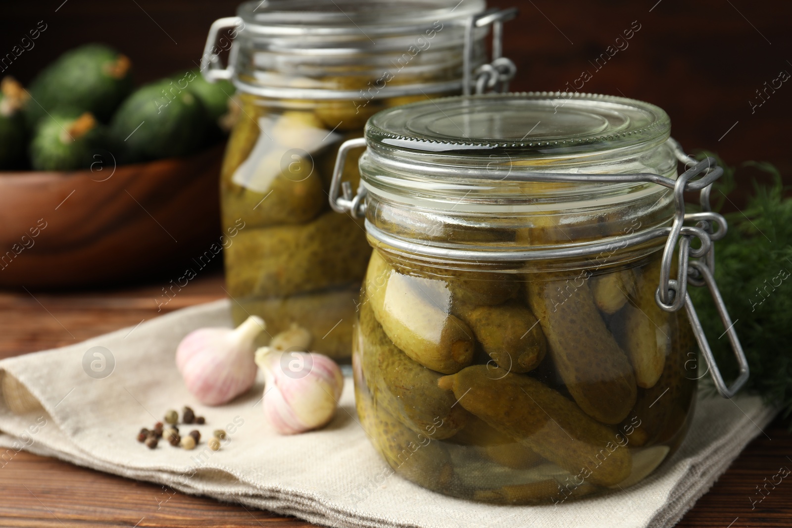 Photo of Pickled cucumbers in jars, garlic, dill and peppercorns on wooden table, closeup