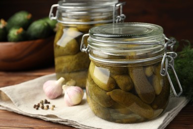 Photo of Pickled cucumbers in jars, garlic, dill and peppercorns on wooden table, closeup