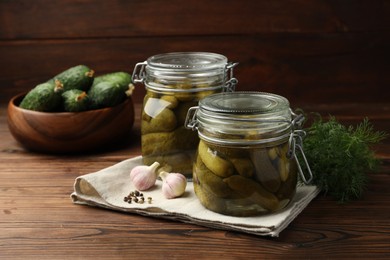 Pickled cucumbers in jars, garlic, dill and peppercorns on wooden table