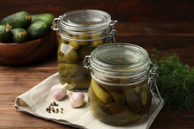 Photo of Pickled cucumbers in jars, garlic, dill and peppercorns on wooden table