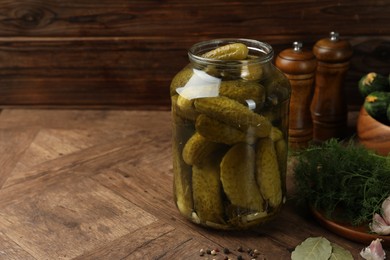 Pickled cucumbers in jar, vegetables and spices on wooden table. Space for text