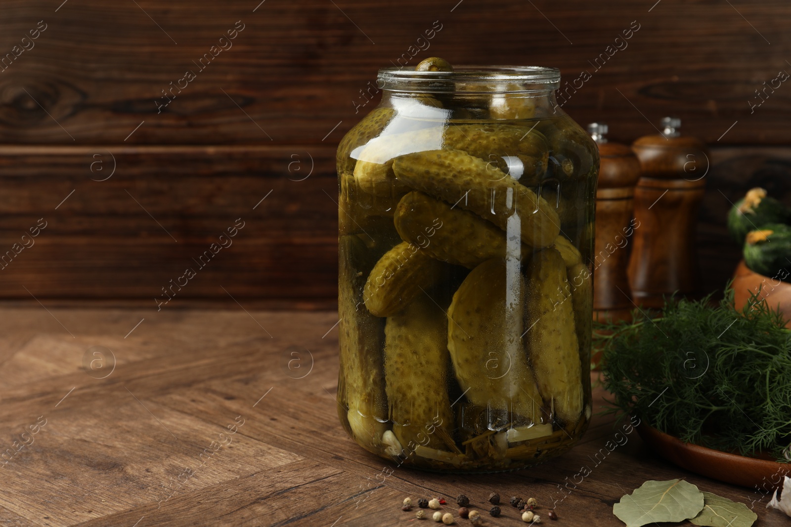 Photo of Pickled cucumbers in jar, vegetables and spices on wooden table. Space for text