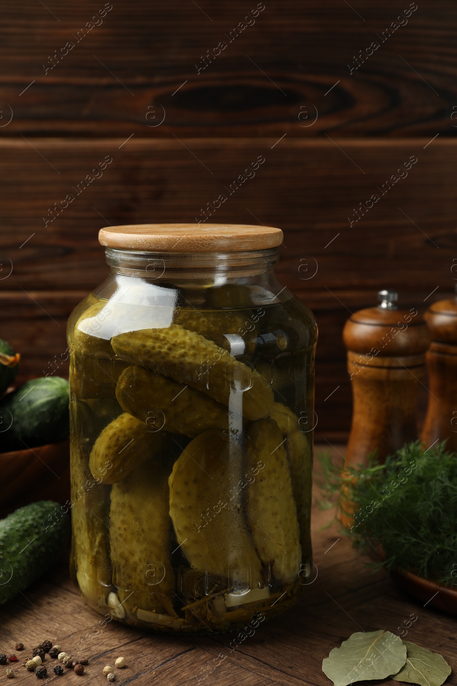 Photo of Pickled cucumbers in jar, vegetables and spices on wooden table