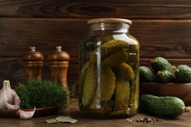 Pickled cucumbers in jar, vegetables and spices on wooden table, closeup