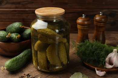 Pickled cucumbers in jar, vegetables and spices on wooden table, closeup