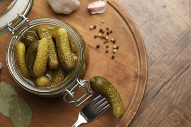 Pickled cucumbers in open jar and spices on wooden table, top view. Space for text