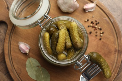 Pickled cucumbers in open jar and spices on wooden table, top view