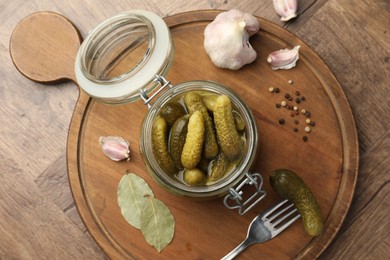 Pickled cucumbers in open jar and spices on wooden table, top view