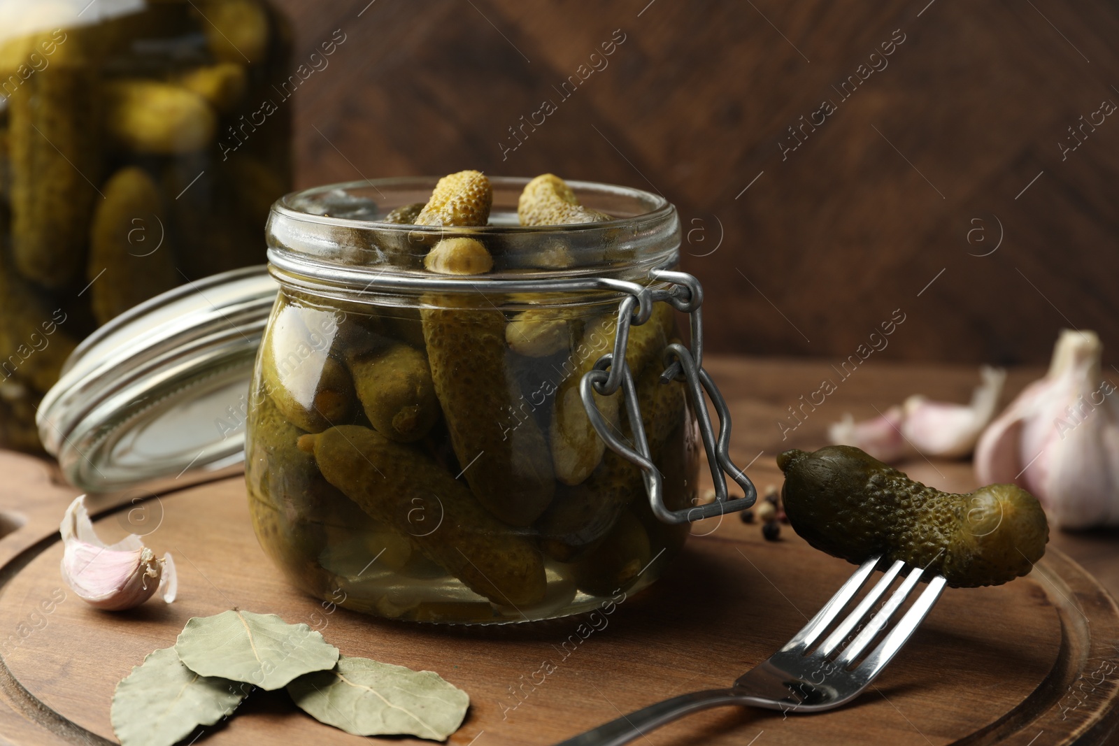 Photo of Pickled cucumbers in open jar, fork and spices on wooden table, closeup