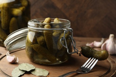 Pickled cucumbers in open jar, fork and spices on wooden table, closeup