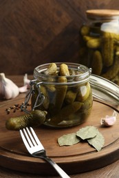 Pickled cucumbers in open jar, fork and spices on wooden table