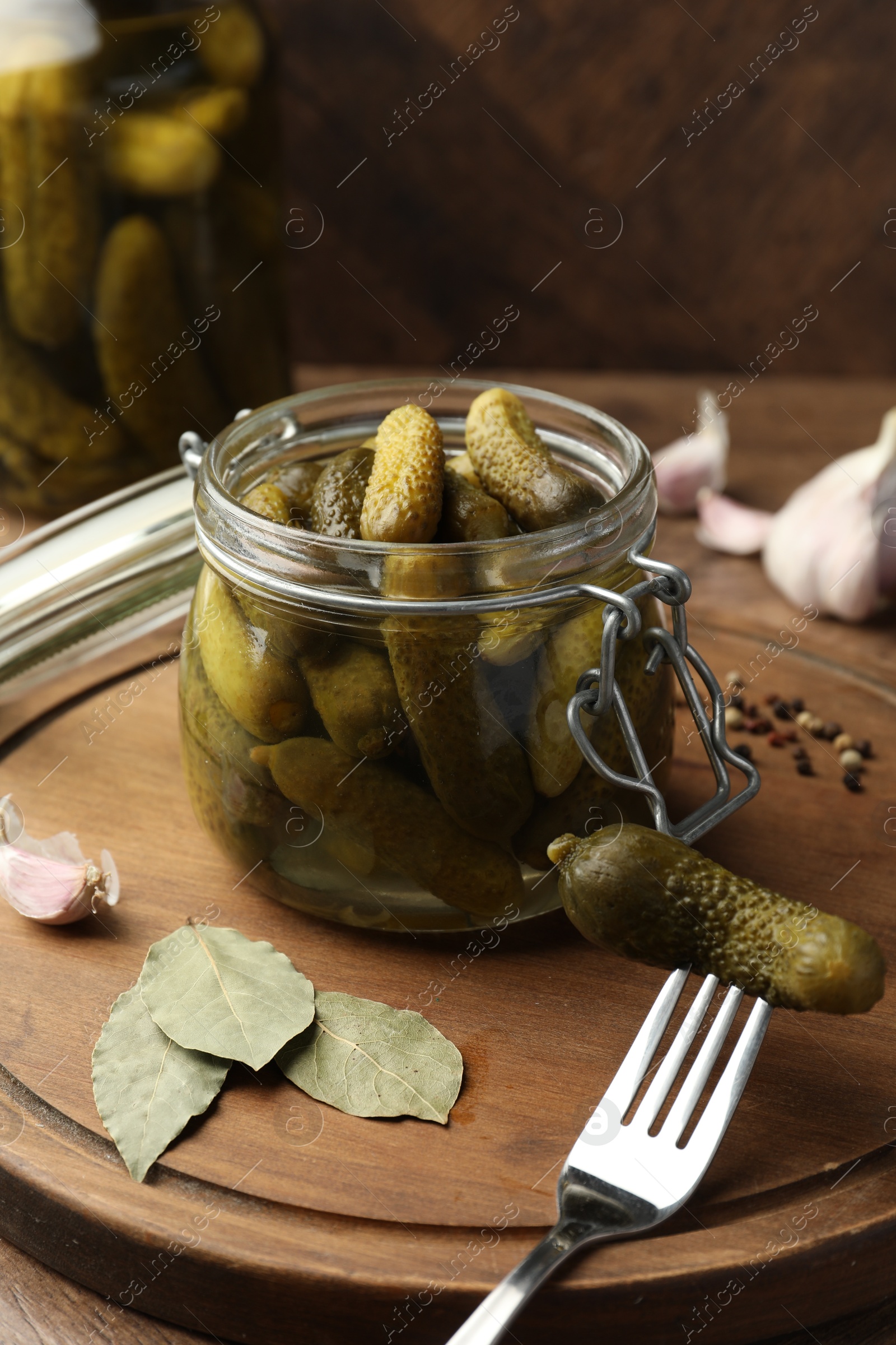 Photo of Pickled cucumbers in open jar, fork and spices on wooden table, closeup