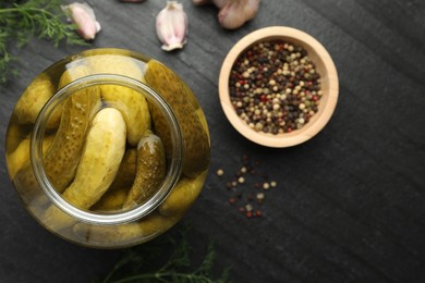 Pickled cucumbers in open jar and spices on dark textured table, flat lay