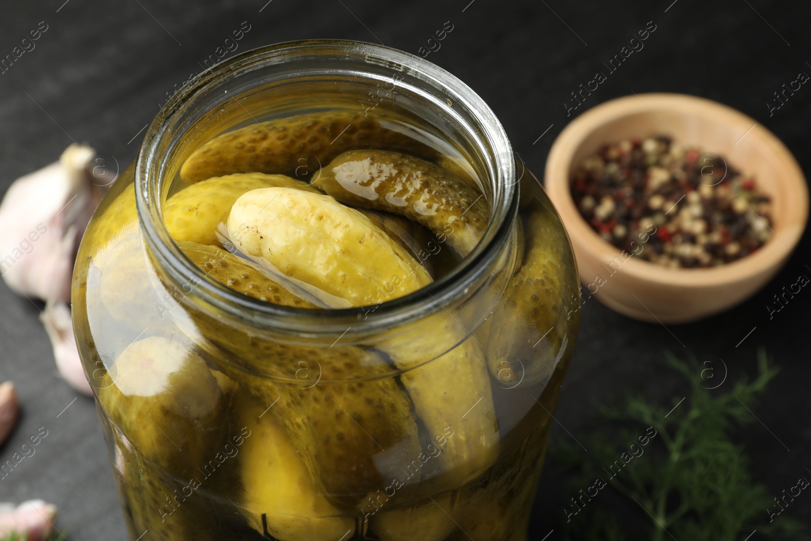 Photo of Pickled cucumbers in open jar and spices on dark table, closeup