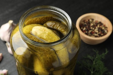 Pickled cucumbers in open jar and spices on dark table, closeup