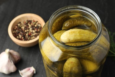 Pickled cucumbers in open jar and spices on dark table, closeup