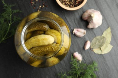 Pickled cucumbers in open jar and spices on dark textured table, flat lay