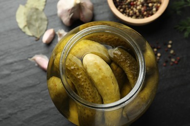 Pickled cucumbers in open jar and spices on dark textured table, above view