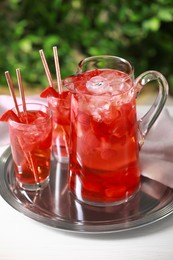 Photo of Tasty strawberry lemonade in jug and glasses on white table against blurred green background