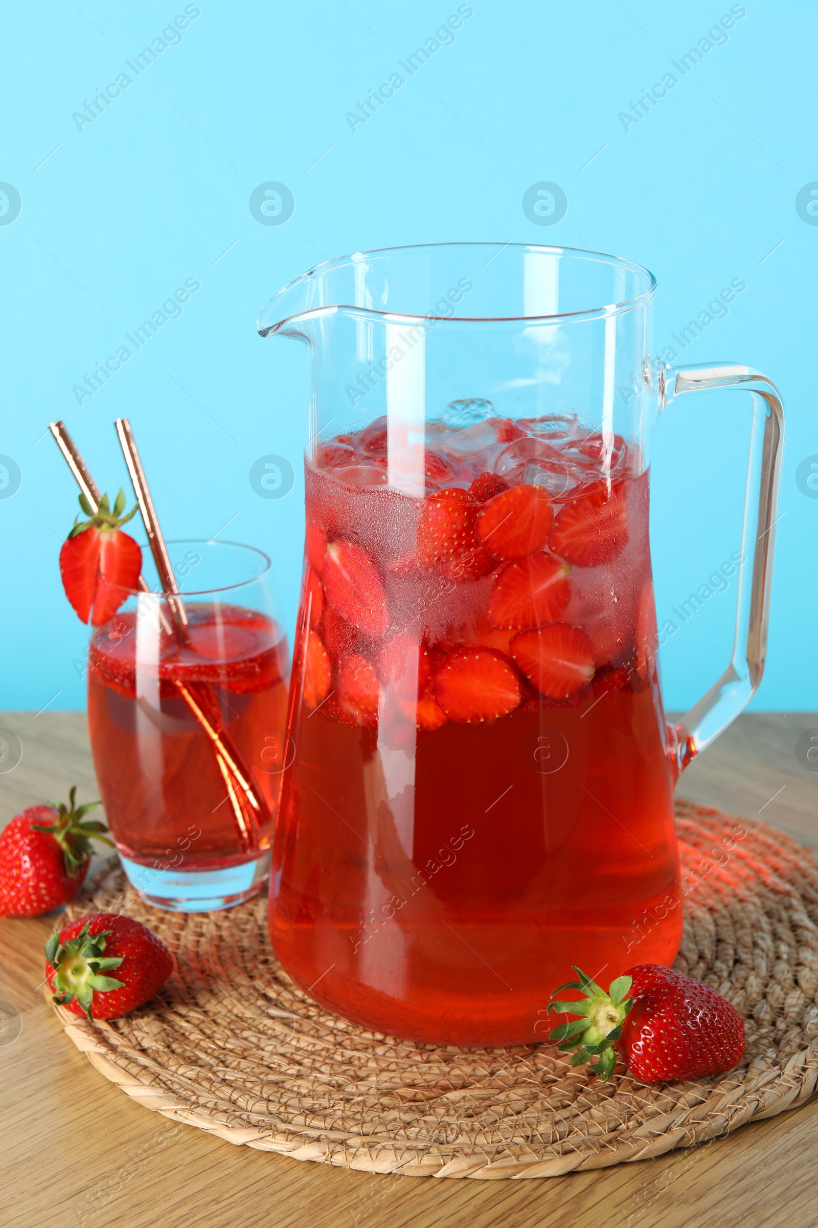 Photo of Tasty strawberry lemonade in jug, glass and berries on wooden table against light blue background