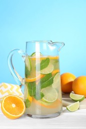 Photo of Freshly made lemonade with mint in jug on white wooden table against light blue background