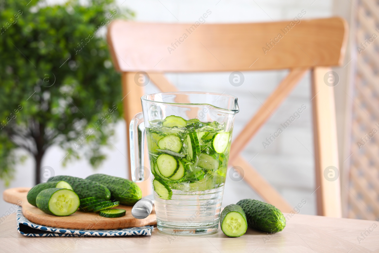 Photo of Refreshing cucumber water in jug and vegetables on light wooden table. Space for text