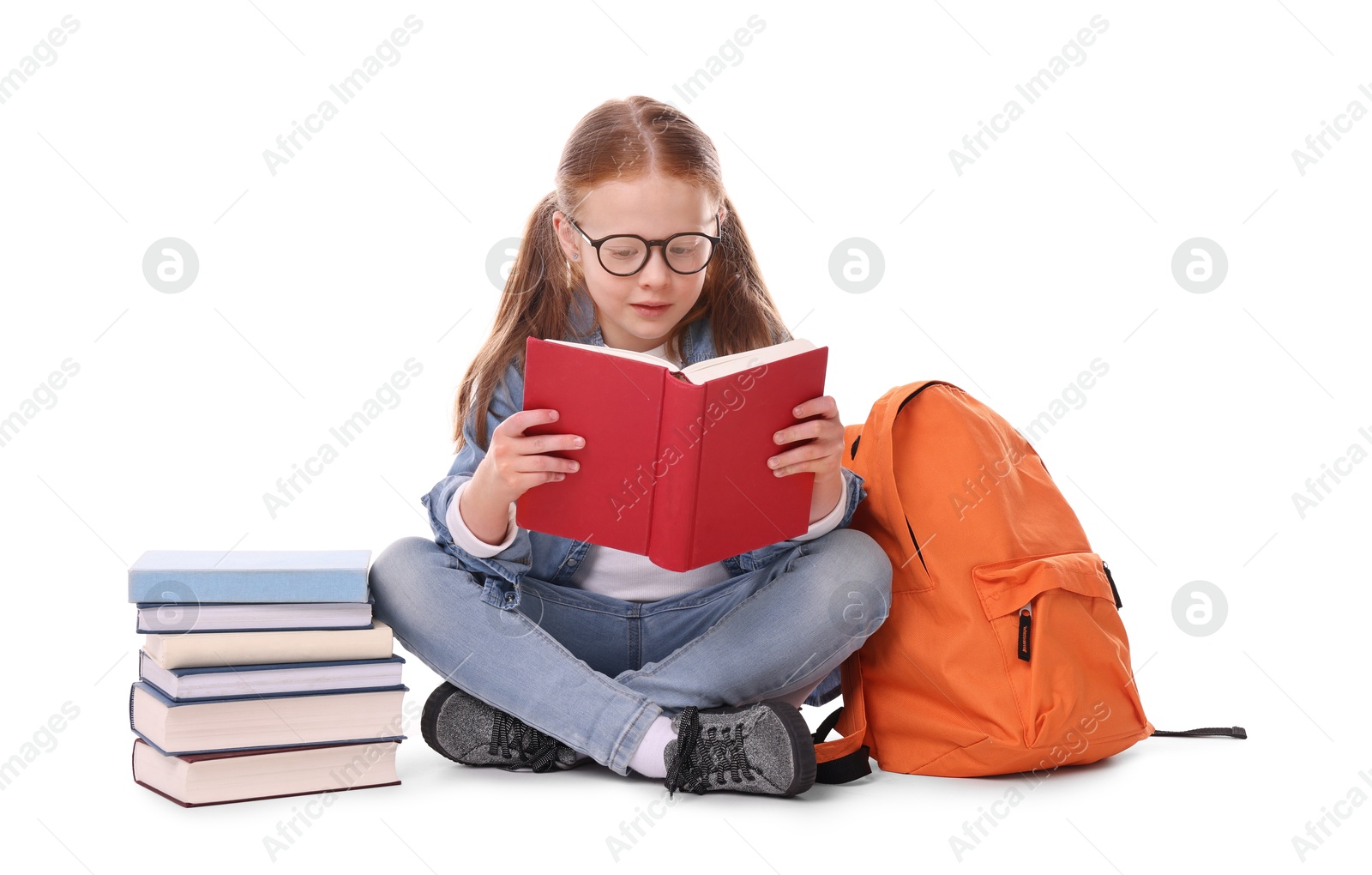 Photo of Cute little girl reading book near backpack on white background