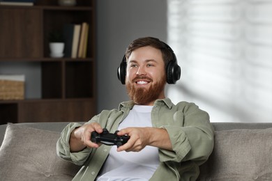 Photo of Happy man in headphones playing video game with controller at home