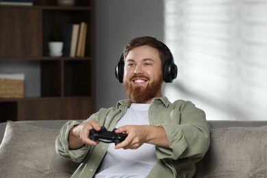 Happy man in headphones playing video game with controller at home