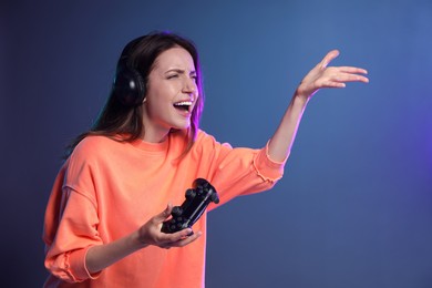 Emotional woman in headphones with game controller on dark blue background. Space for text