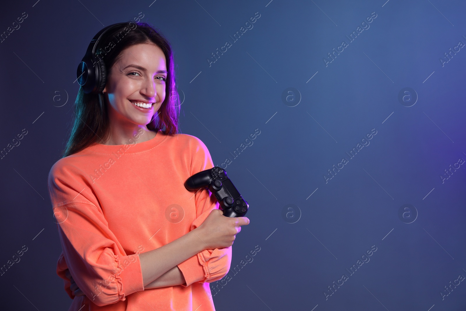 Photo of Happy woman in headphones with game controller on dark blue background. Space for text