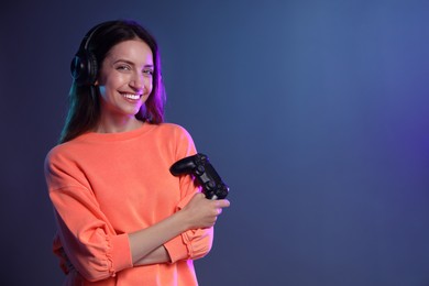 Photo of Happy woman in headphones with game controller on dark blue background. Space for text