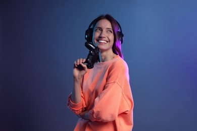 Photo of Happy woman in headphones with game controller on dark blue background