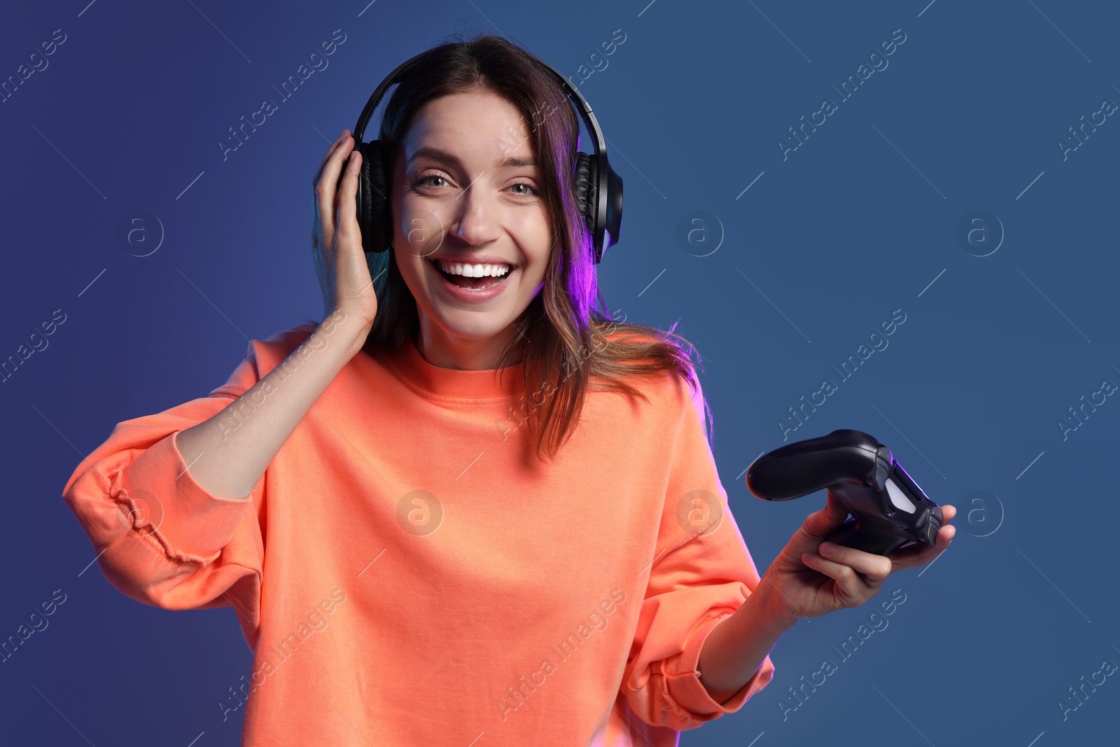 Photo of Happy woman in headphones with game controller on dark blue background