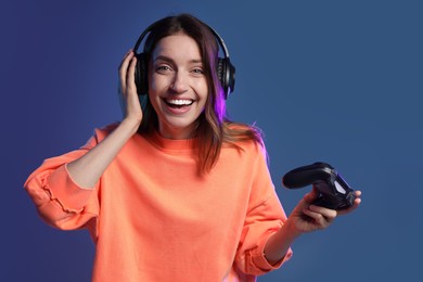 Photo of Happy woman in headphones with game controller on dark blue background