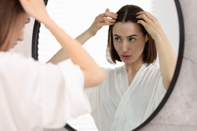 Photo of Young woman with hair loss problem looking at mirror indoors